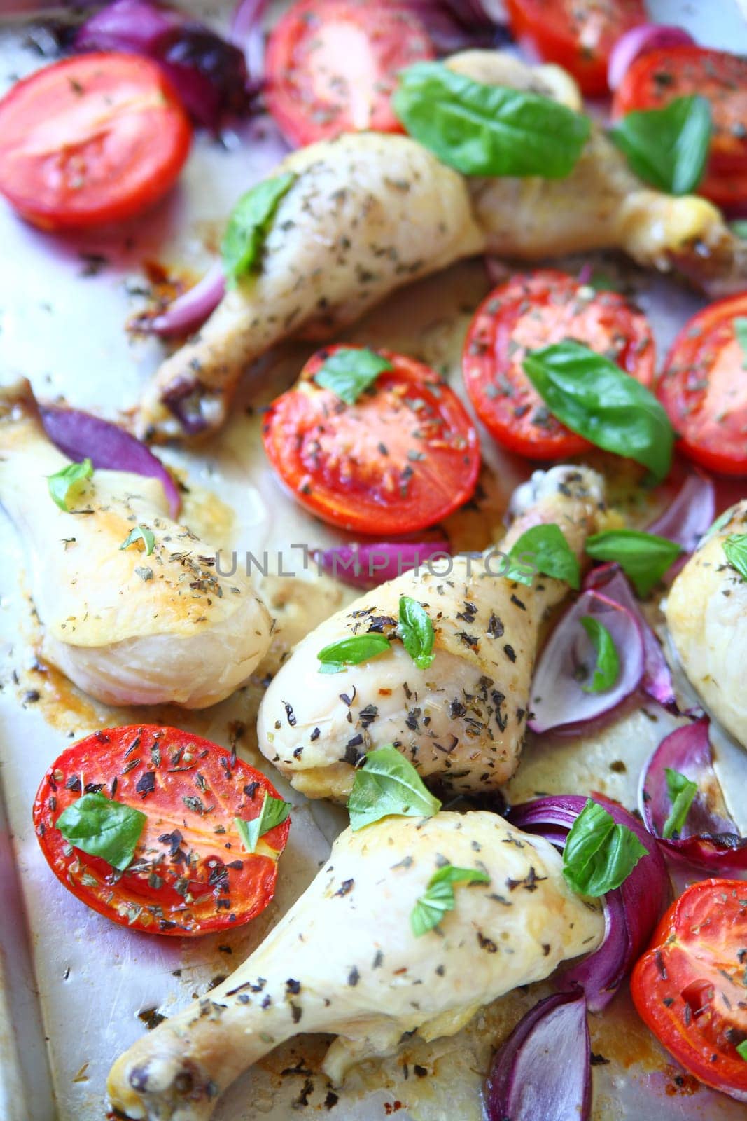 Vertical view of chicken legs, Roma tomatoes and basil on sheet pan