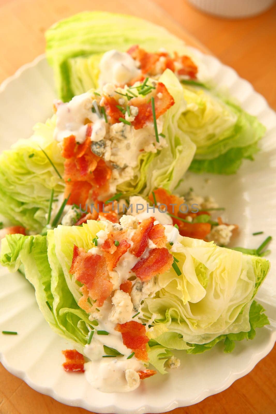 Vertical view of lettuce wedges topped with blue cheese dressing, bacon and chives