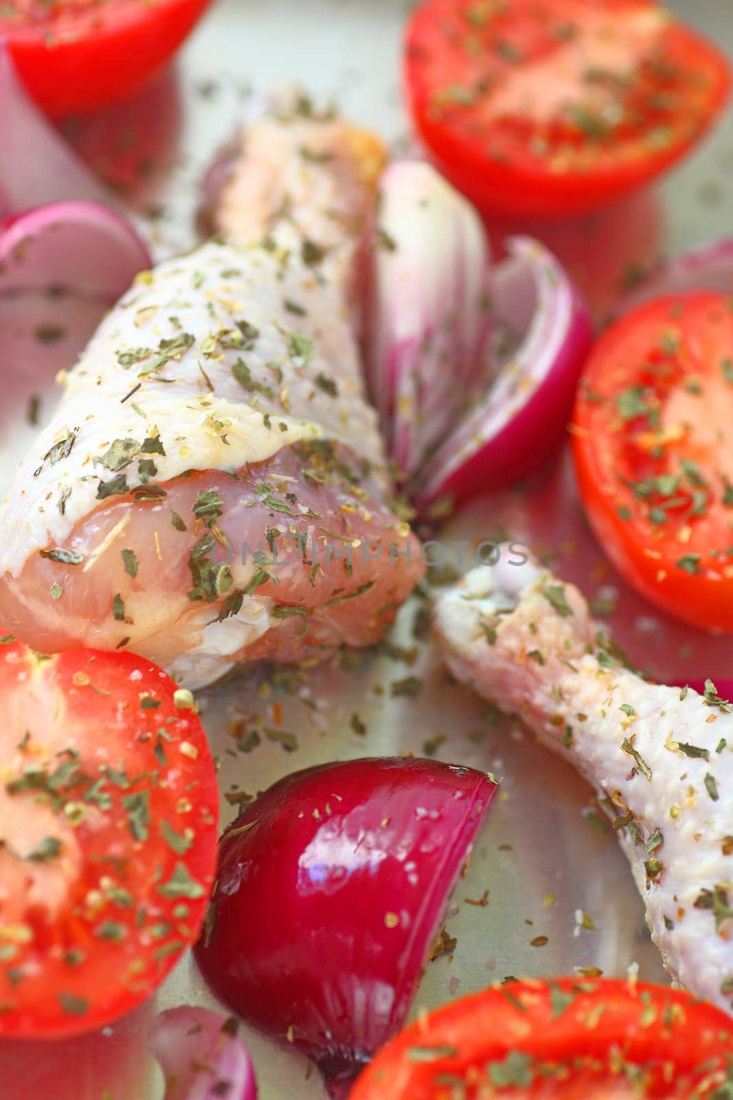 Vertical view of uncooked chicken dinner with Roma tomatoes and red onion