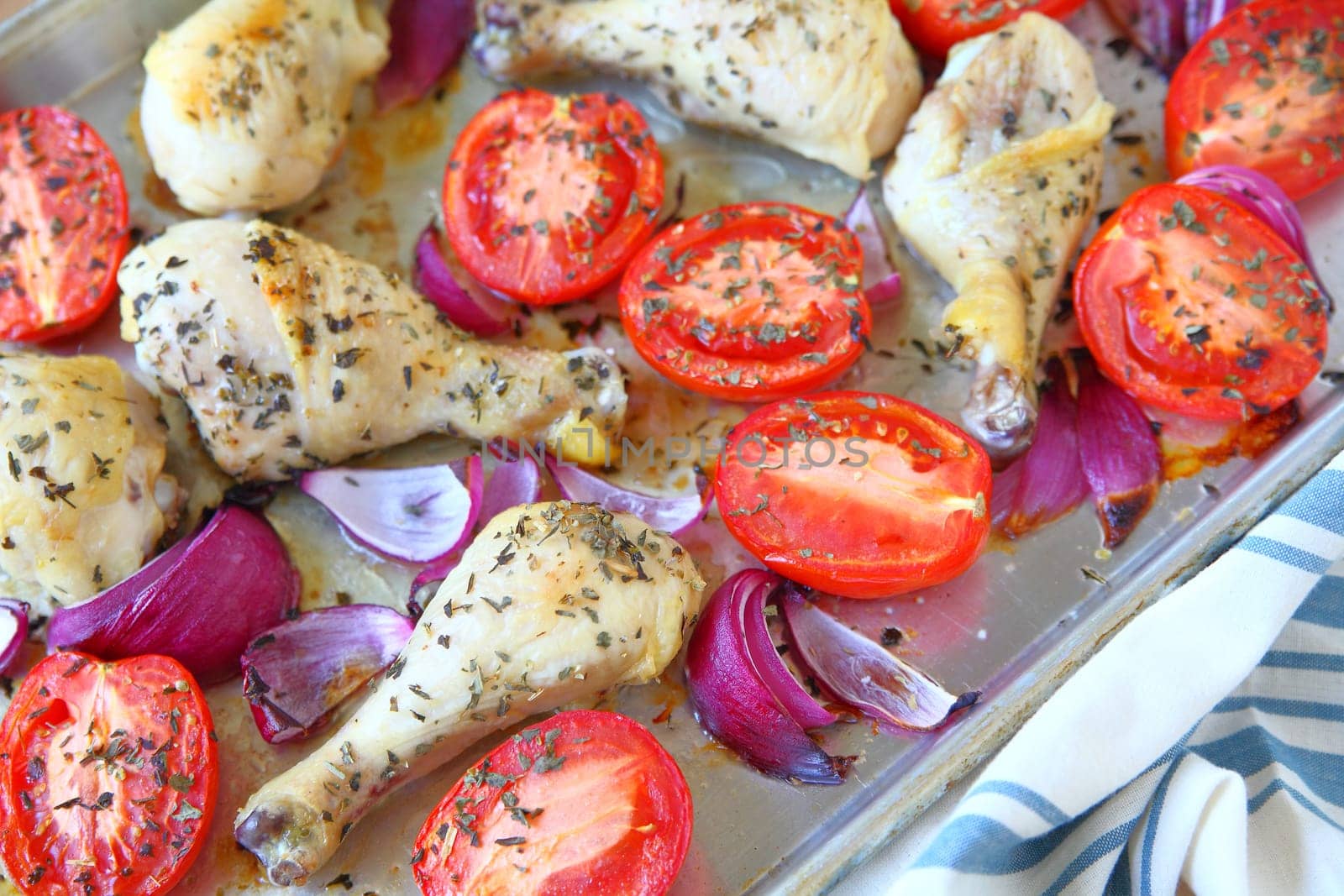Sheet pan dinner of chicken, Roma tomatoes and red onions with dish towel