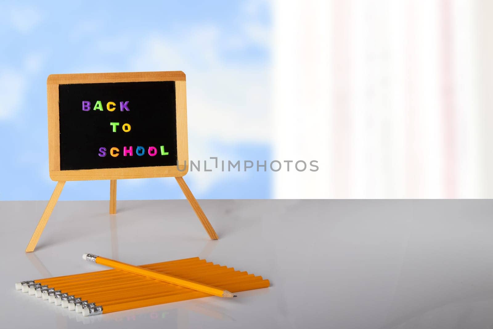 Back to school written with colorful letters on blackboard, and yellow pencils are lying on table in front of bright background. Concept education. Space for your text or display product montage.