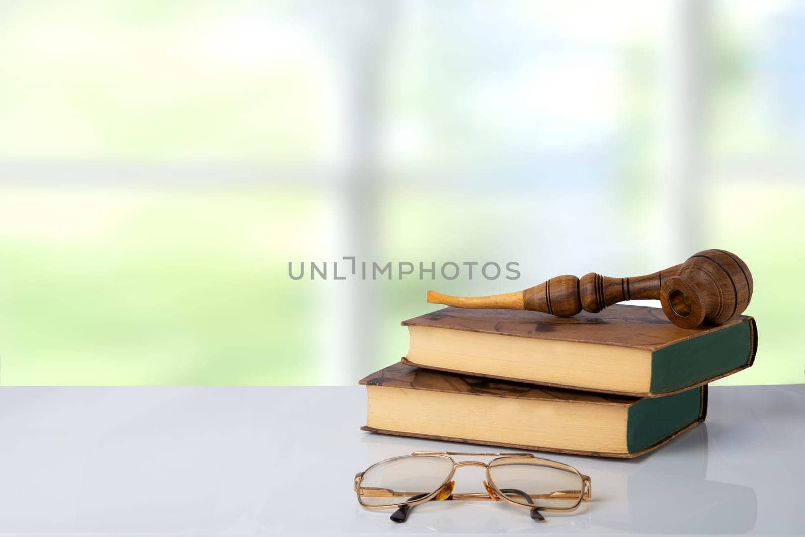 Two old books with a tobacco pipe on them and a pair of glasses in front of bright background. The teachers day. Back to school. Space.