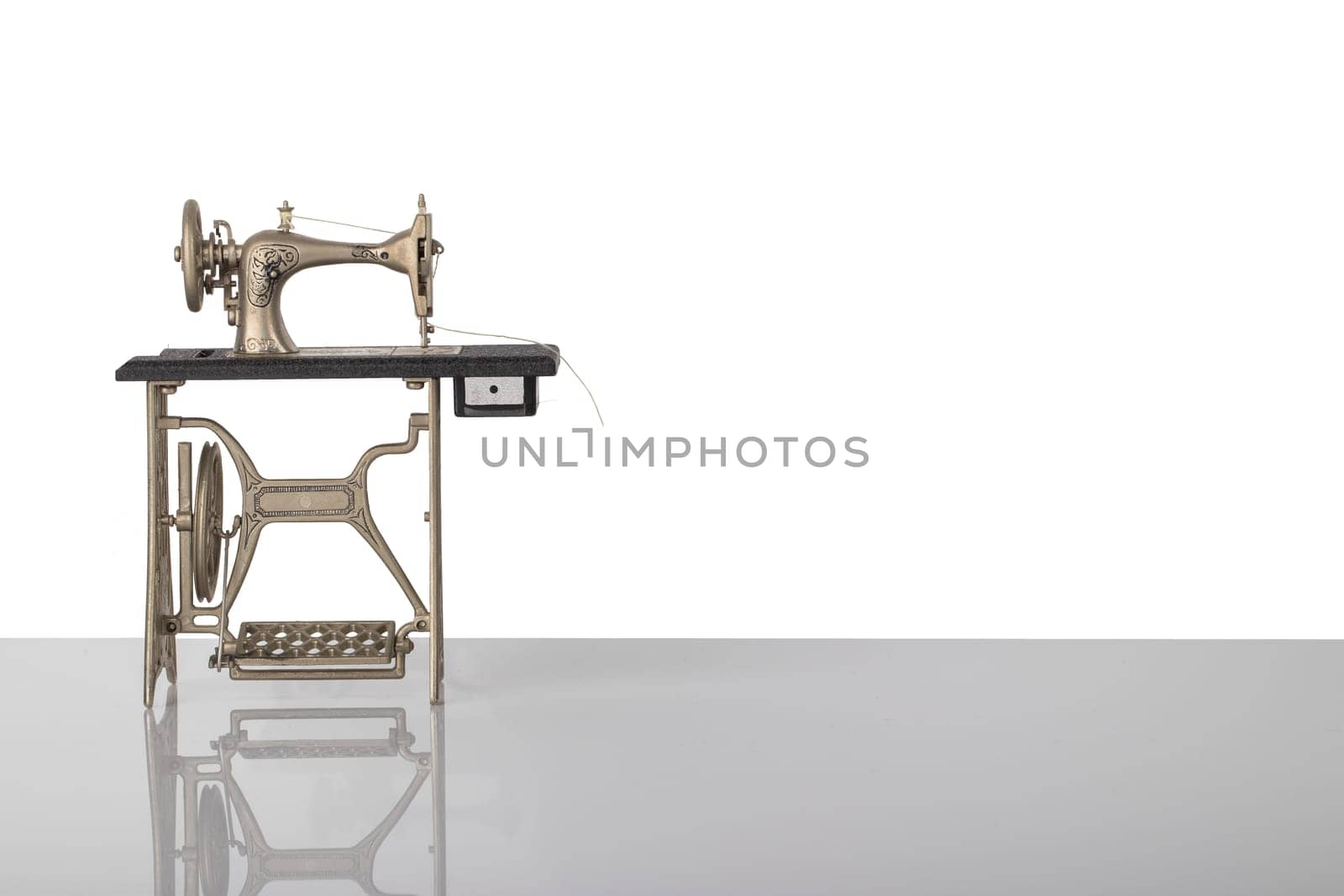 Beautiful miniature model of a vintage sewing machine on bright table isolated on white background. Advertisement for tailor business. Space for text and montage.