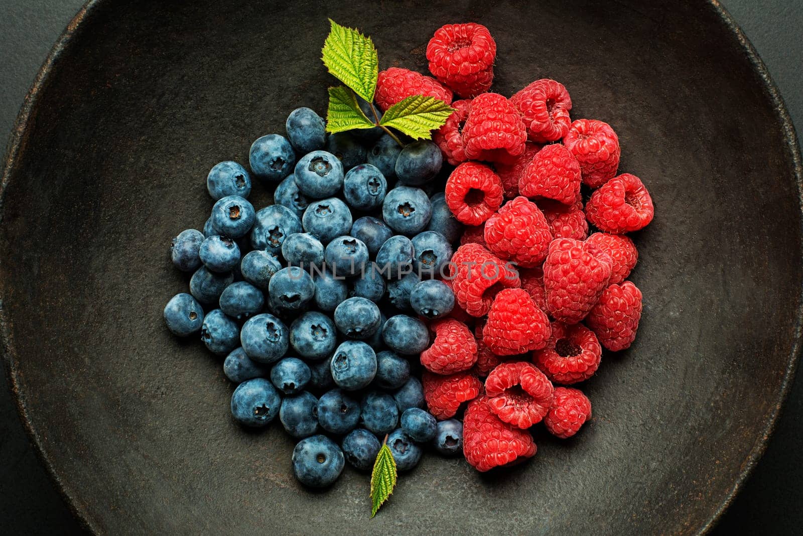 Mix of fresh berries in a bowl on black background