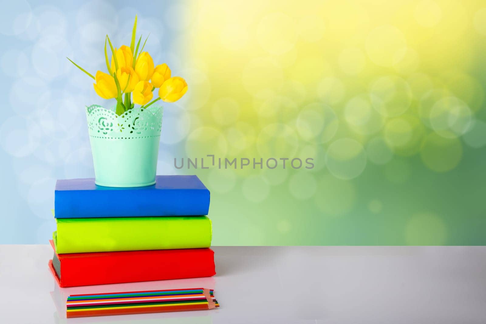 Colorful school equipment and yellow tulips on table against bright yellow bokeh background. Concept education.