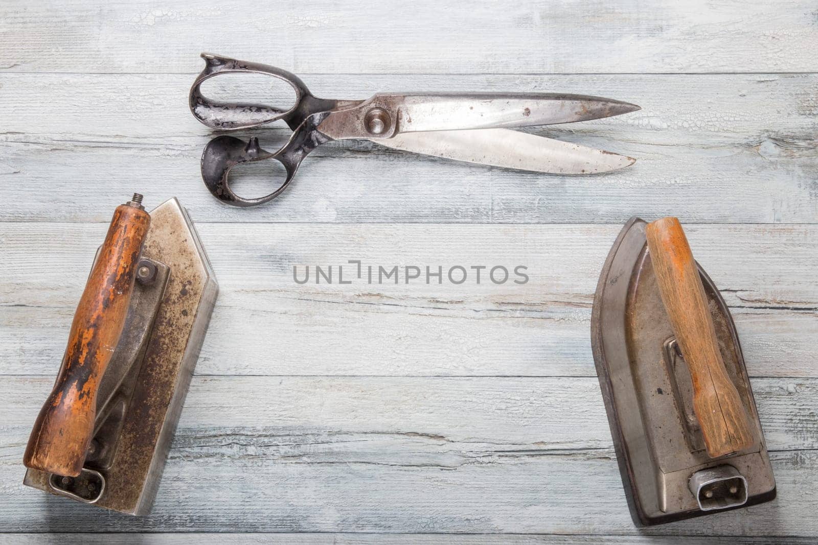 Professional old large tailor irons and one large scissors on rustic wooden table. Tailoring accessories.