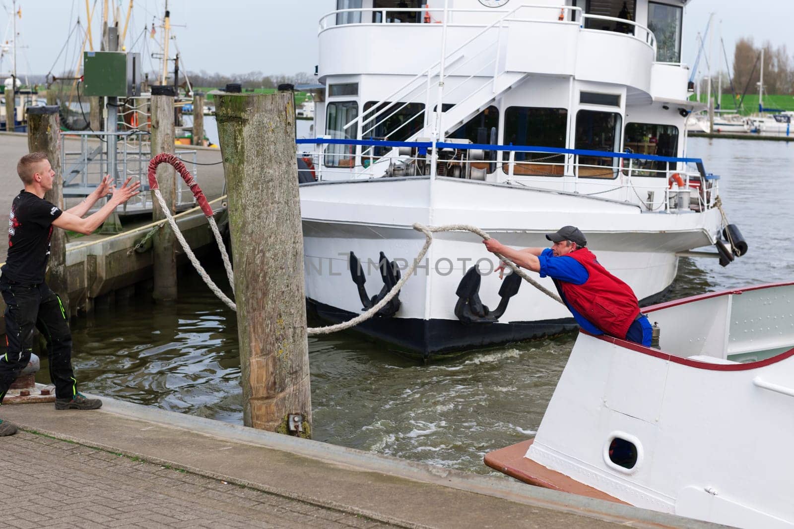 Carolinensiel, Germany - April 17, 2018: Mooring maneuver with two boatsmen of a passenger ship in the harbor of Carolinensiel. Boatmen throw themselves
