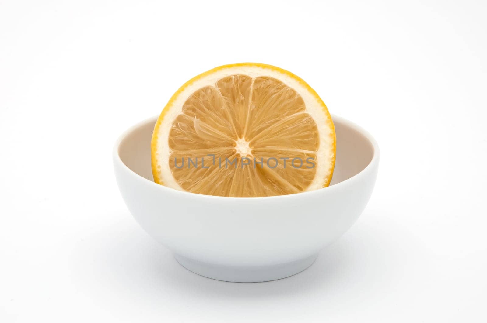 A half lemon in a white ceramics cup on a white background is isolated.