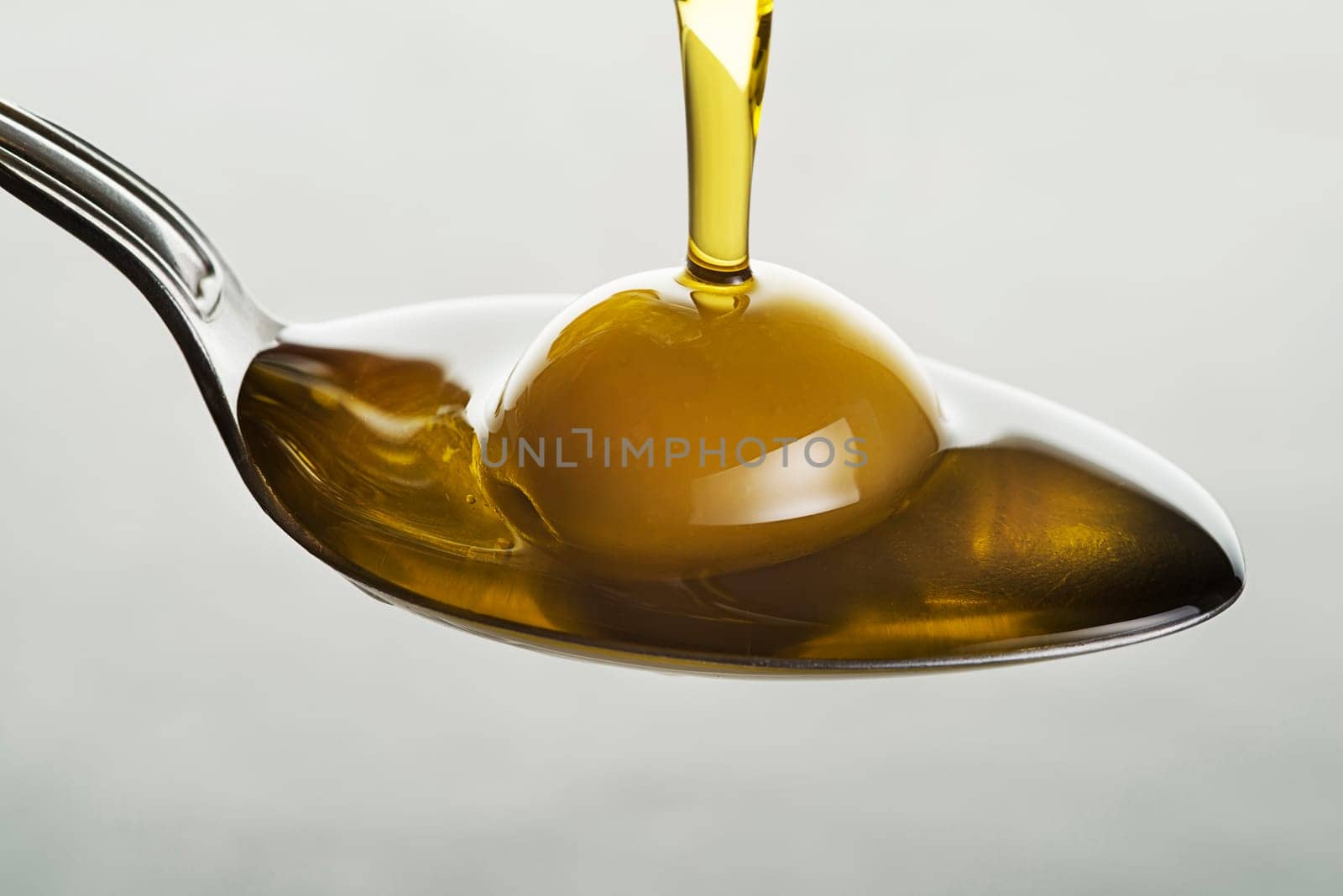 Bottle of virgin olive oil pouring to the spoon close up
