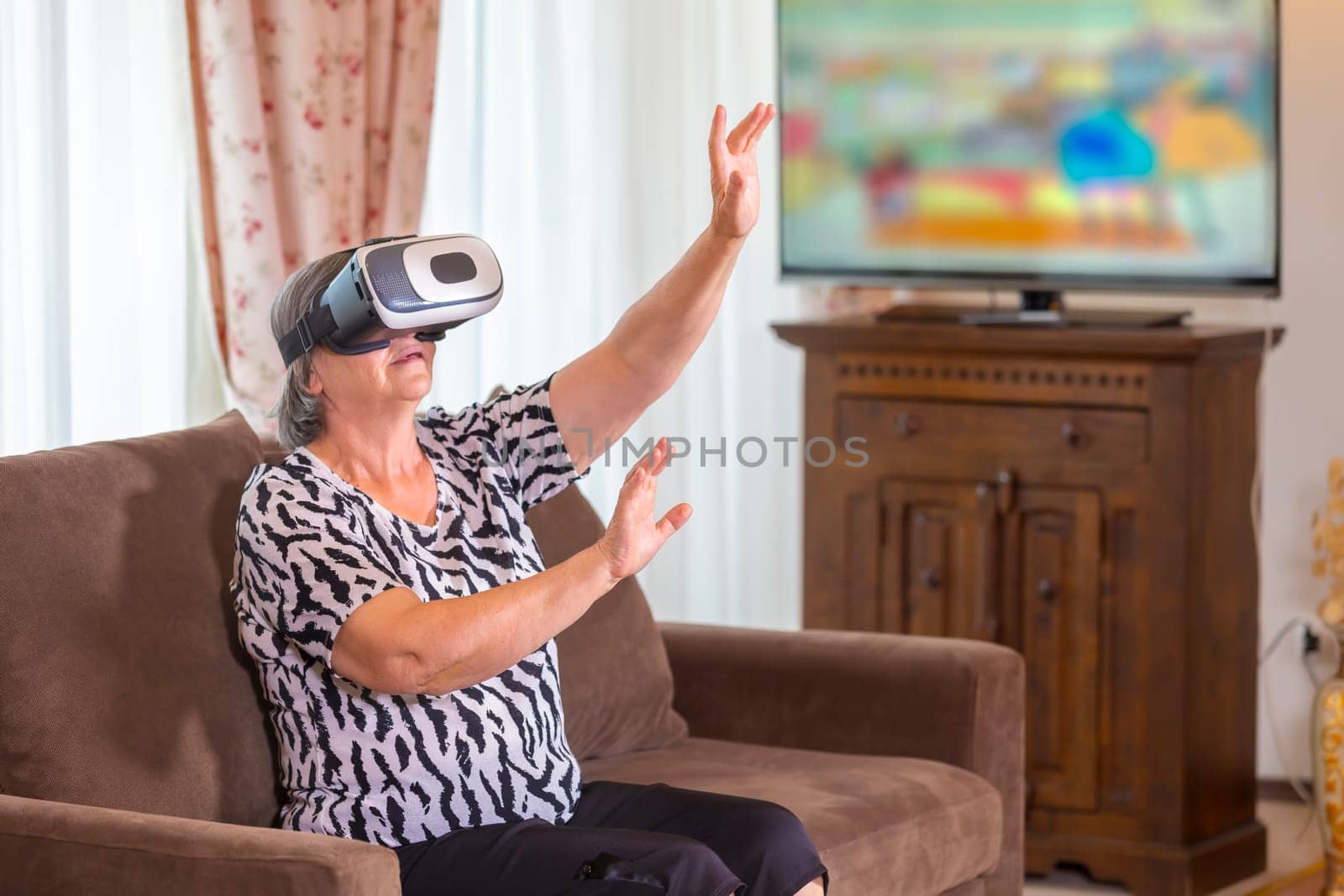 Senior woman with virtual headset or 3d glasses playing videogame at home. Technology, augmented reality, entertainment and people concept. Focus on her hands!
