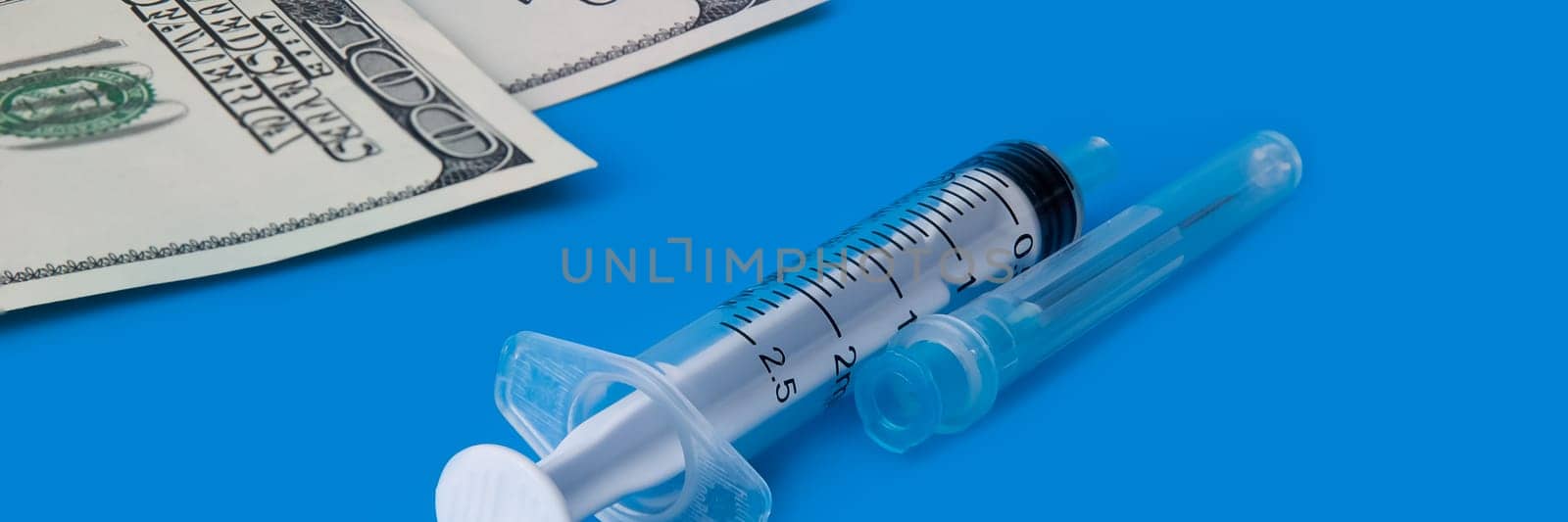 A syringe, and one hundred dollar bills on a blue background.
