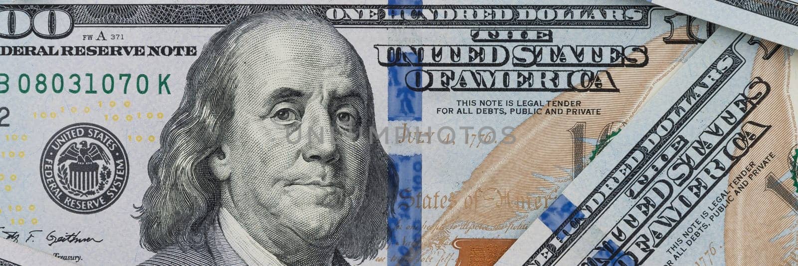 Denominations of one hundred US dollars. Spread out on the table. Not full visibility of notes.