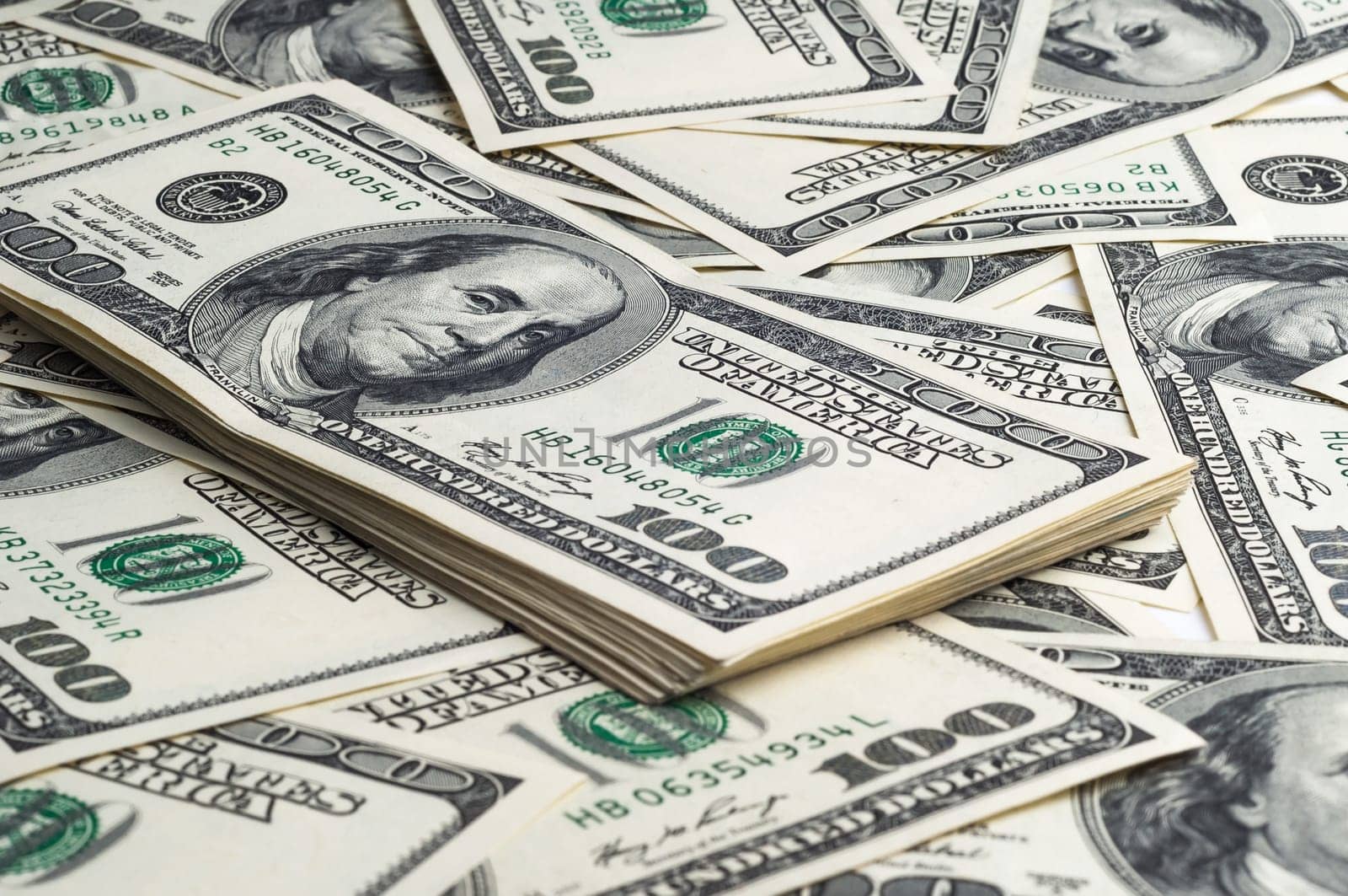 A pack of one hundred dollar bills in the background of scattered dollars. View at an angle, from the side.