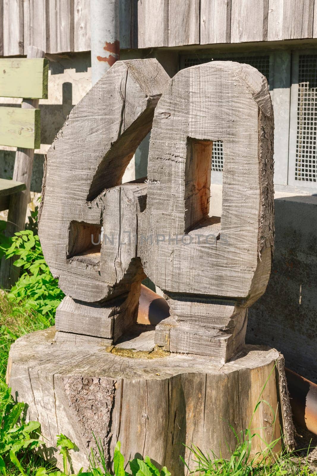 Number 60 carved from a tree stump in front of a barn in the grass.