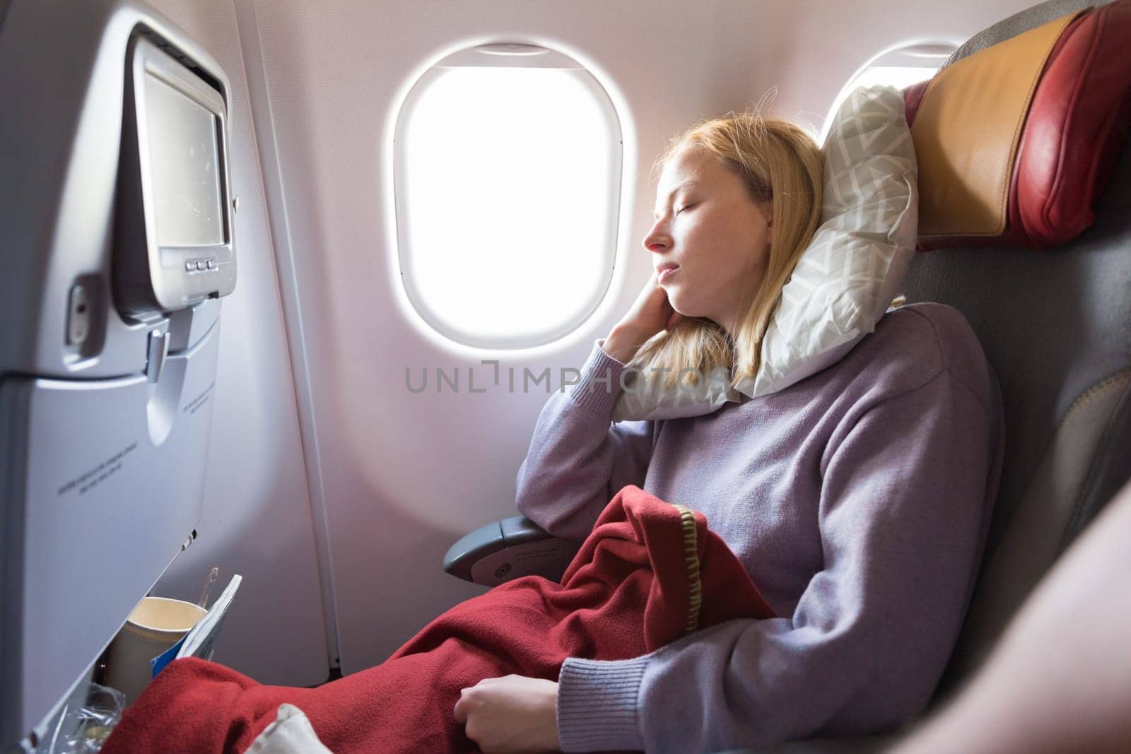 Tired blonde casual caucasian woman sleeping on seat while traveling by airplane on long distance transatlantic flight. Commercial transportation by planes.