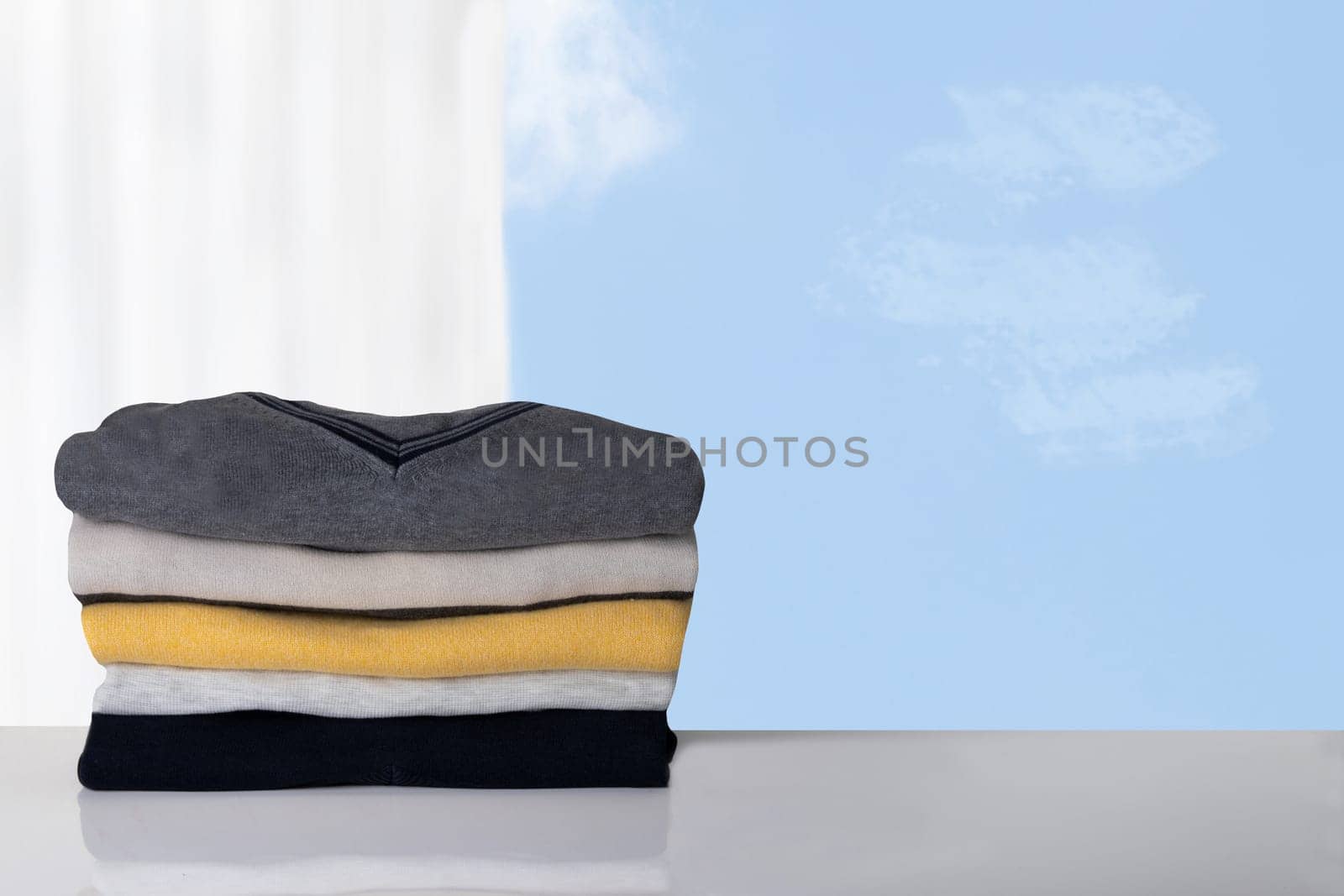 Stack of winter clothes. Pile of colorful cozy warm sweaters against blurred bright background.