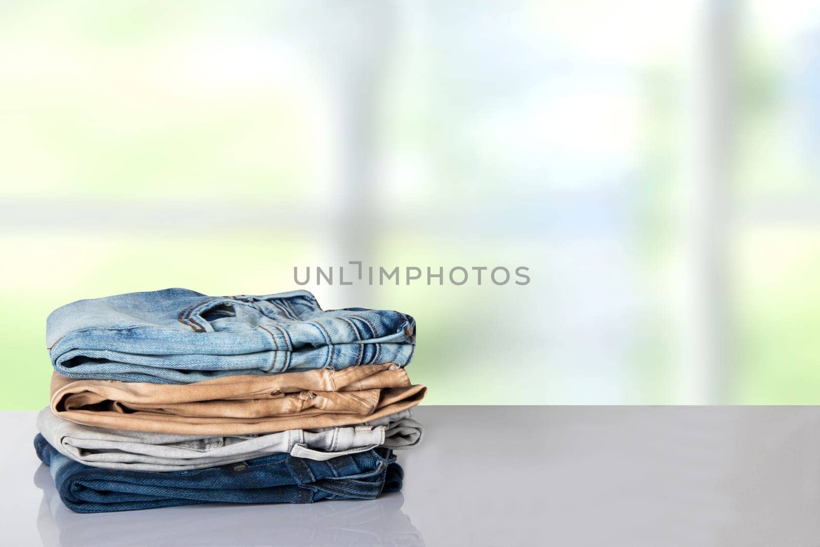 Stack colorful clothes. Pile of colorful jeans on white table with space for your display product montage. Bright background.