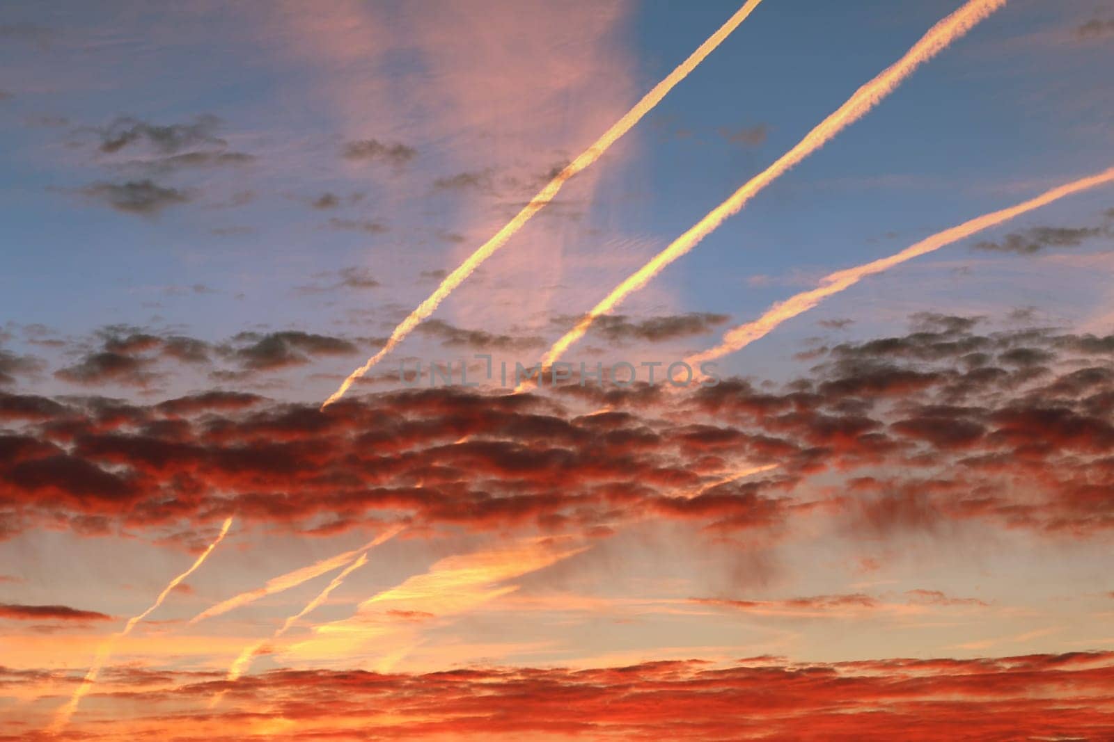 Red morning clouds and streams of condensed vapor on the sky