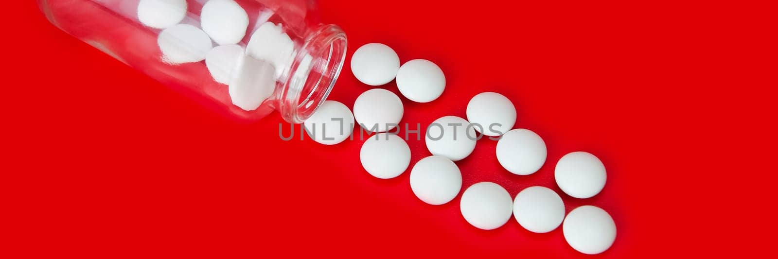 On a red background, white tablets are scattered from a glass bottle.