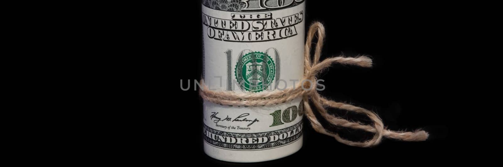 A roll of one hundred dollar bills tied with a rope on a black background. It is located vertically.