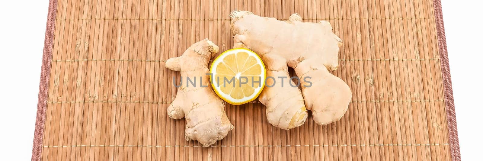 Two pieces of ginger and half a fresh lemon on a bamboo mat.