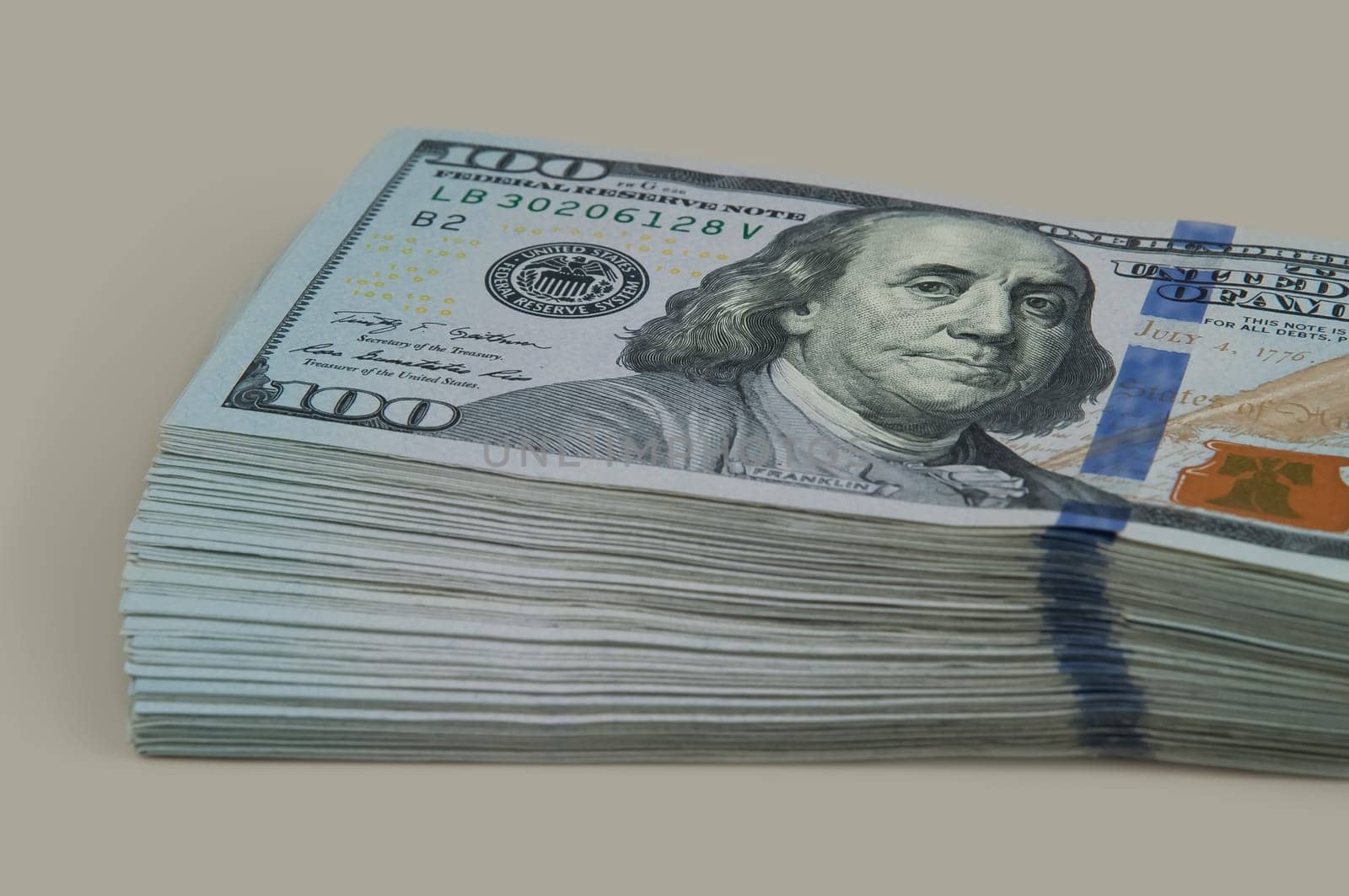 Part of the bundle with a shift of ten thousand dollars in bills of one hundred dollars. On a gray background. View at an angle.