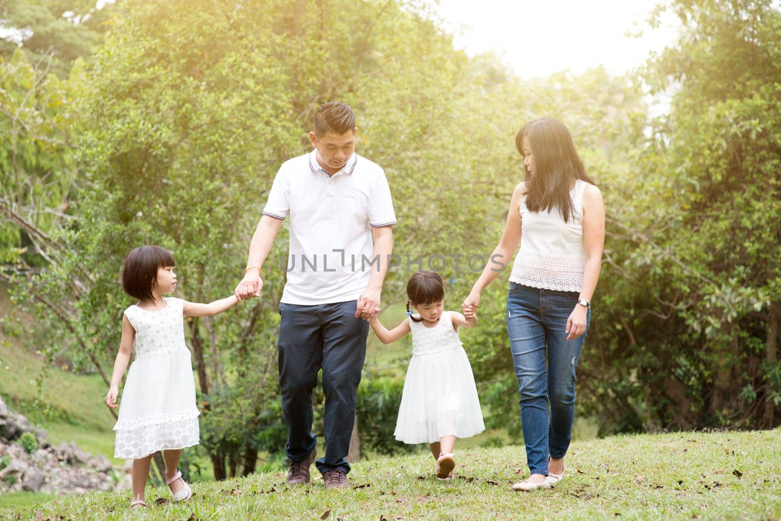 Asian family outdoors. Parents and children holding hands and walking at garden park.