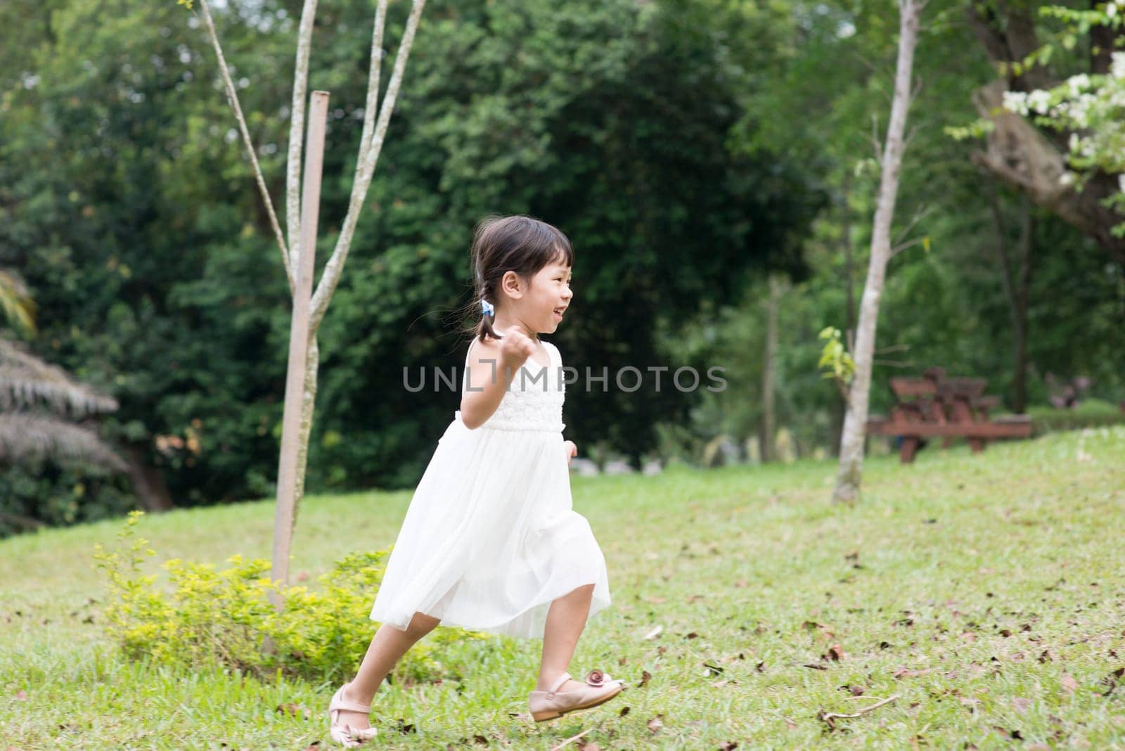 Happy little girl playing and running at green park. Asian family outdoors portrait.