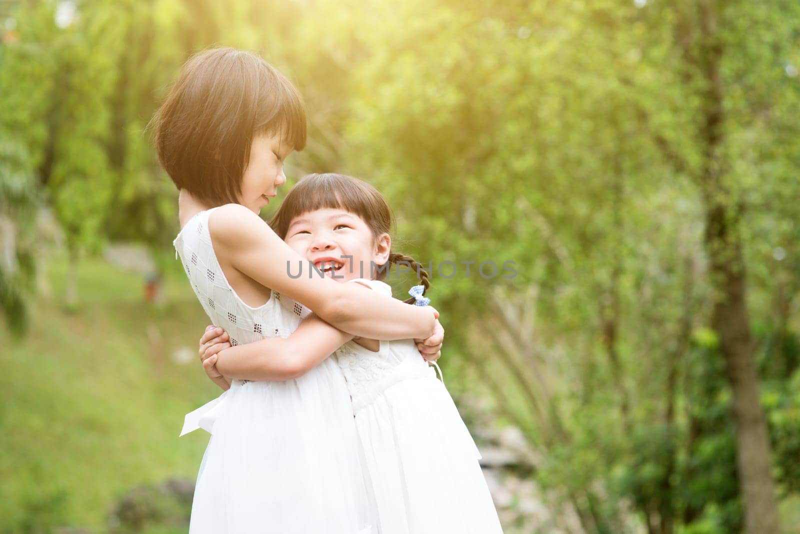 Sisters playing and hugging at garden park. Asian family outdoors portrait.