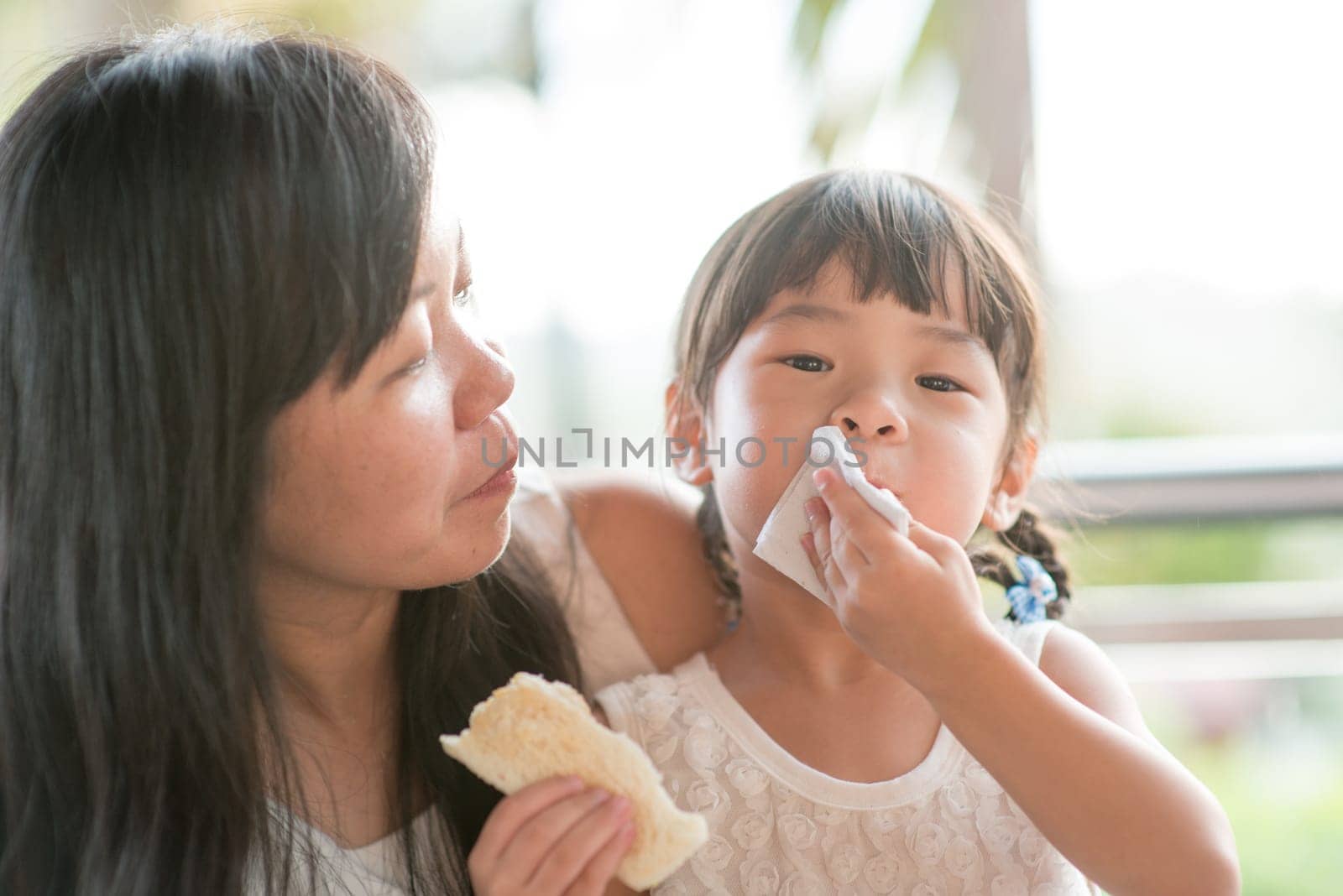 Child wiping her mouth at cafe. Asian family outdoor lifestyle with natural light.