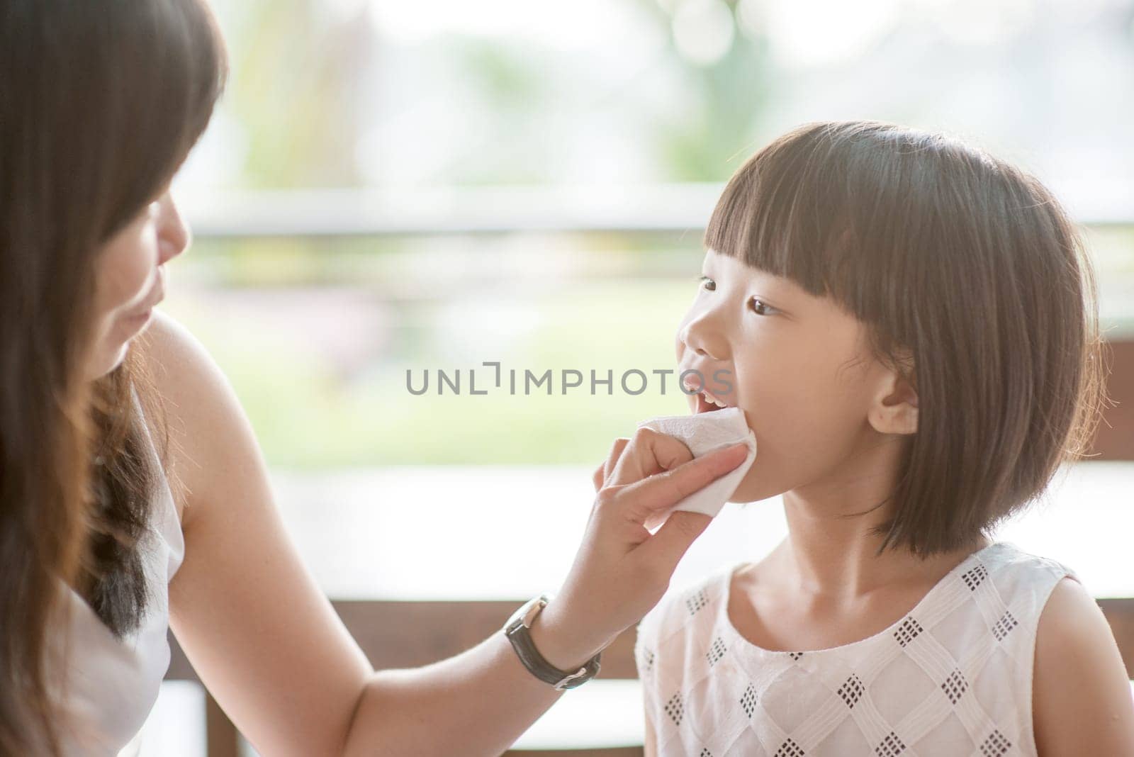 Mom wipes mouth for her child at cafe. Asian family outdoor lifestyle with natural light.