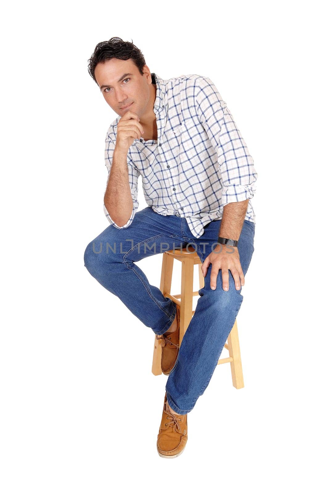 A tall handsome man sitting on a bar chair in a checkered shirt and jeans.with one hand on his chin, isolated for white background.