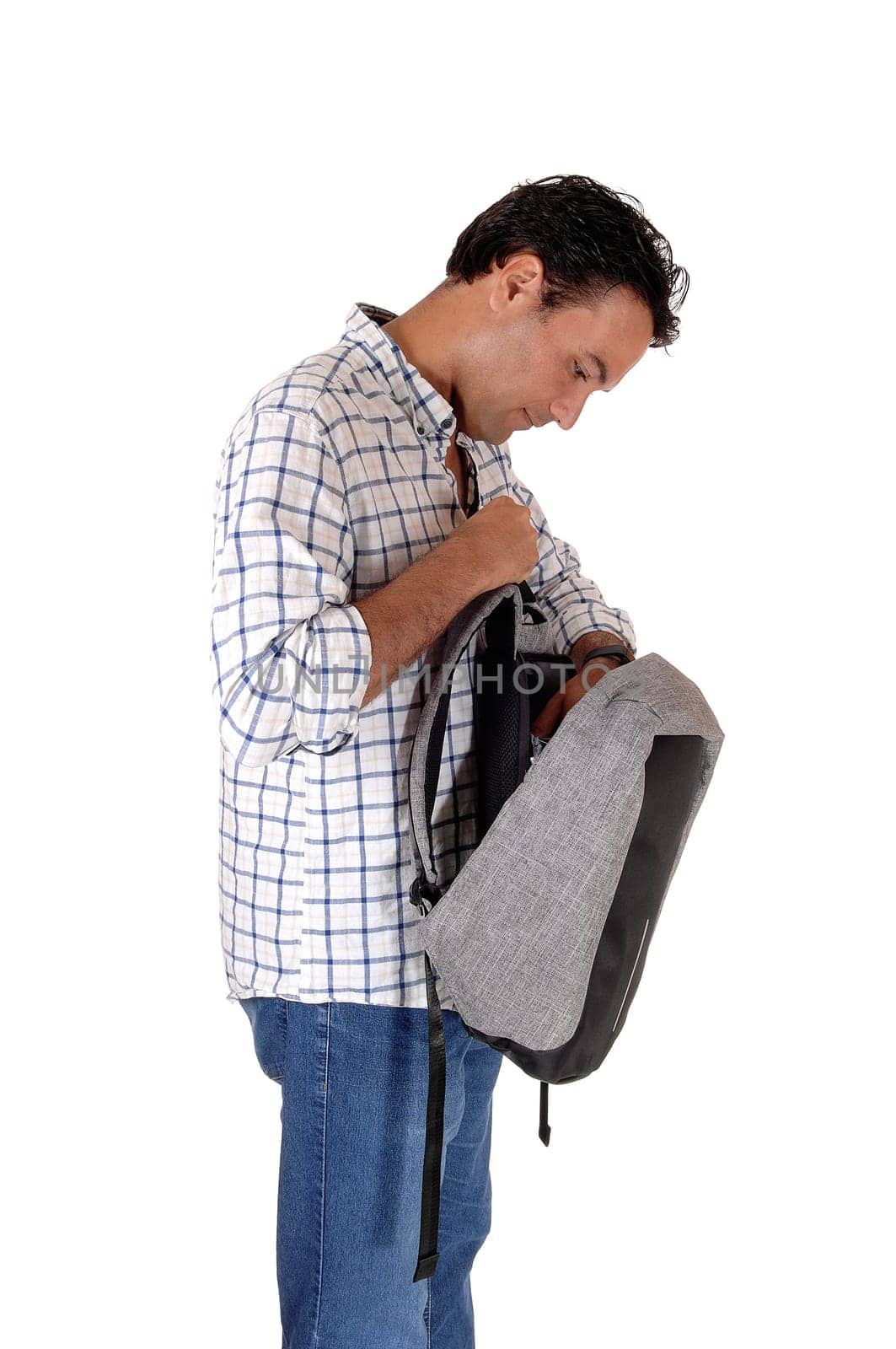 A handsome young man standing in profile looking into his open.backpack, isolated for white background.