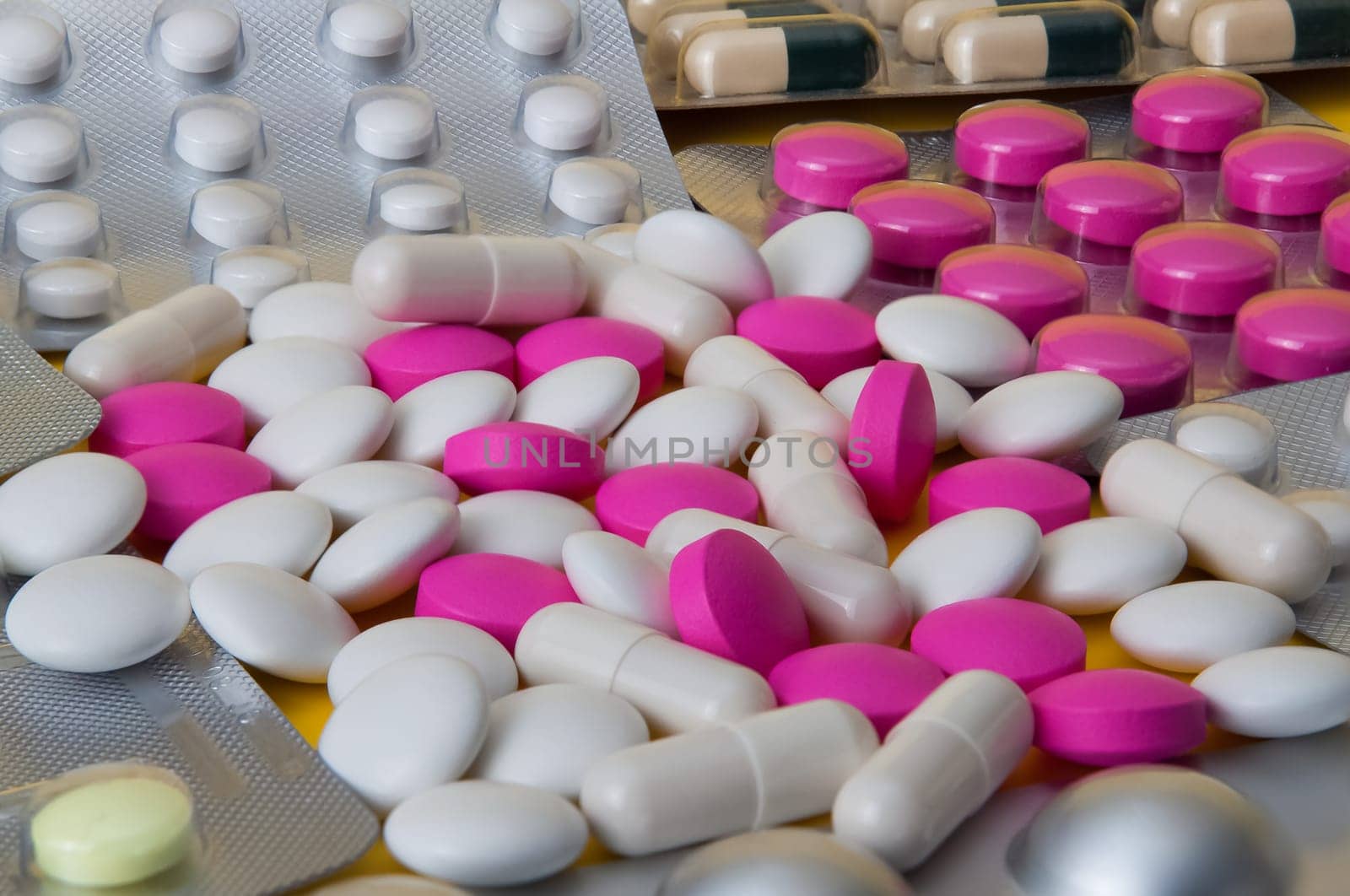 White and pink tablets and blisters with colored pills are scattered. Side view.