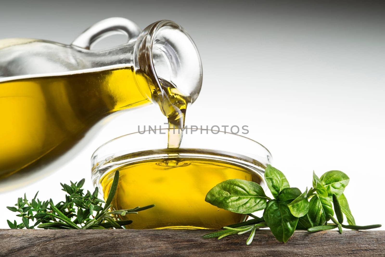 Bottle of virgin olive oil and herbs pouring in a bowl close up
