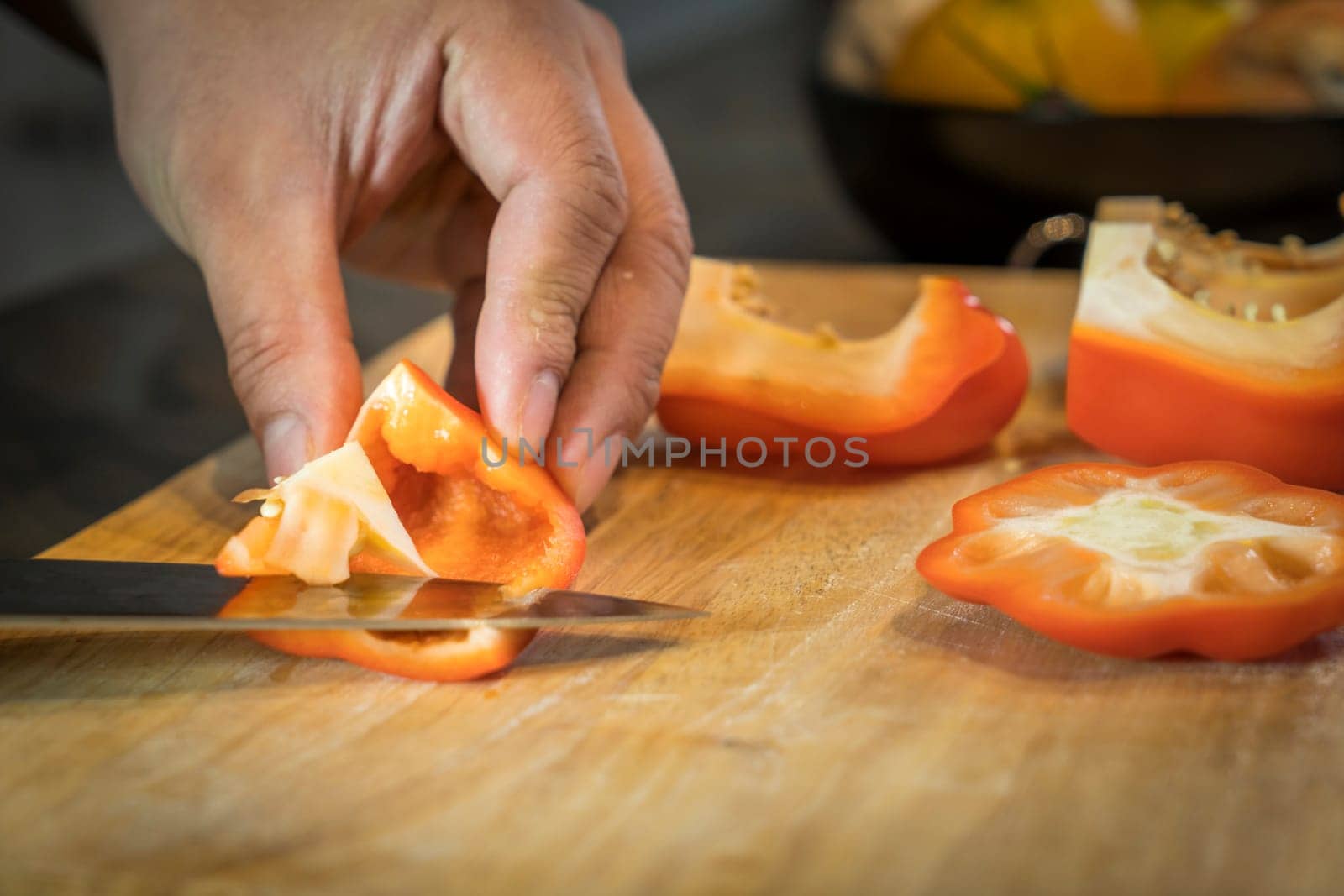 Chef cutting red bell pepper on wooden broad.