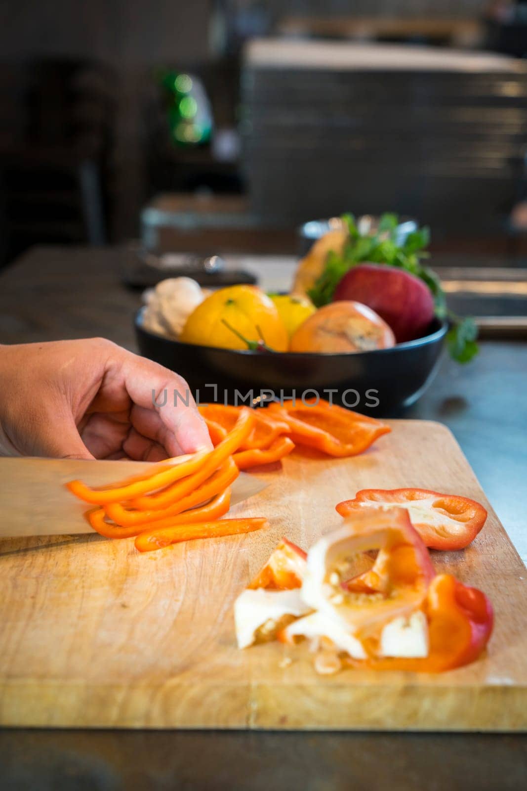 Chef cutting red bell pepper on wooden broad.