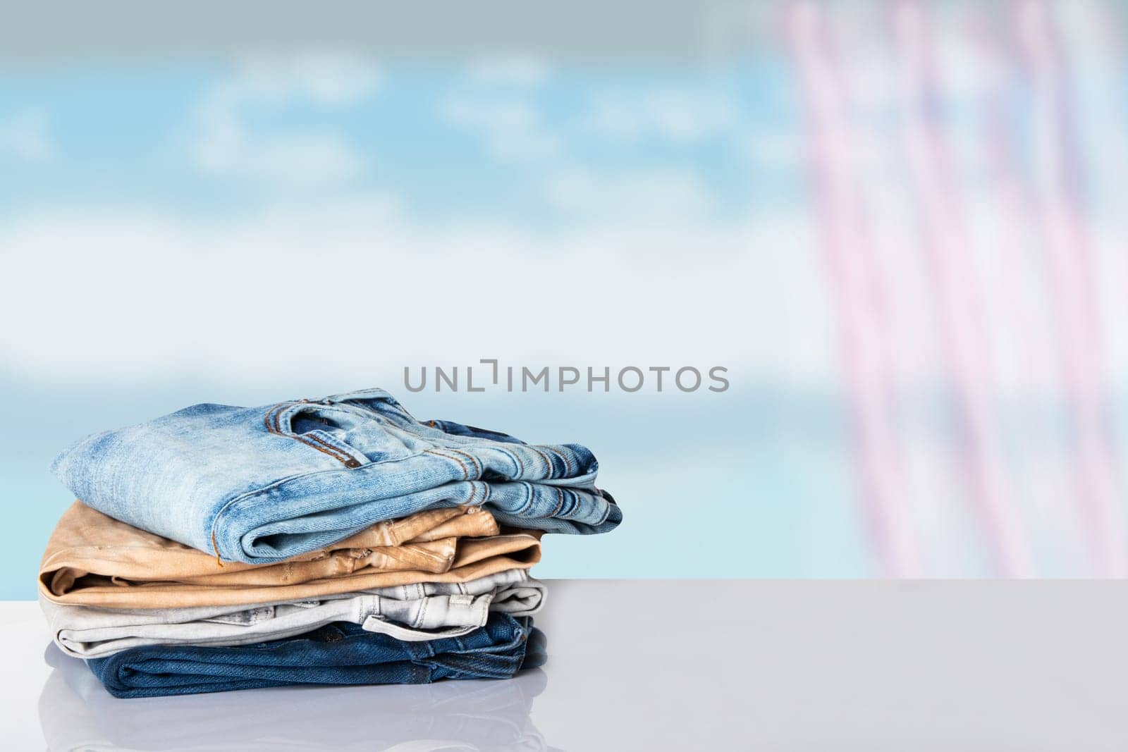 Stack colorful clothes. Pile of colorful jeans on white table with space for your display product montage. Abstract cloudy bright background.