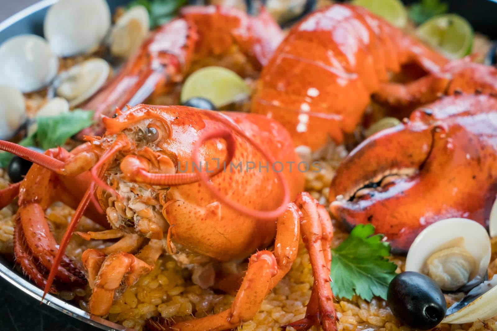Gourmet seafood Valencia paella with fresh langoustine, clams, mussels and squid on savory saffron rice with peas and lemon slices, close up view