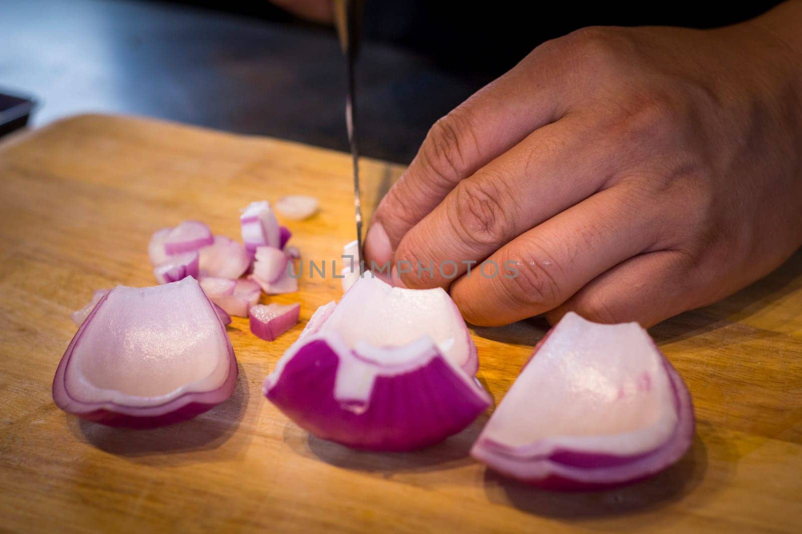 Chef chopping a red onion with a knife on the cutting board.
