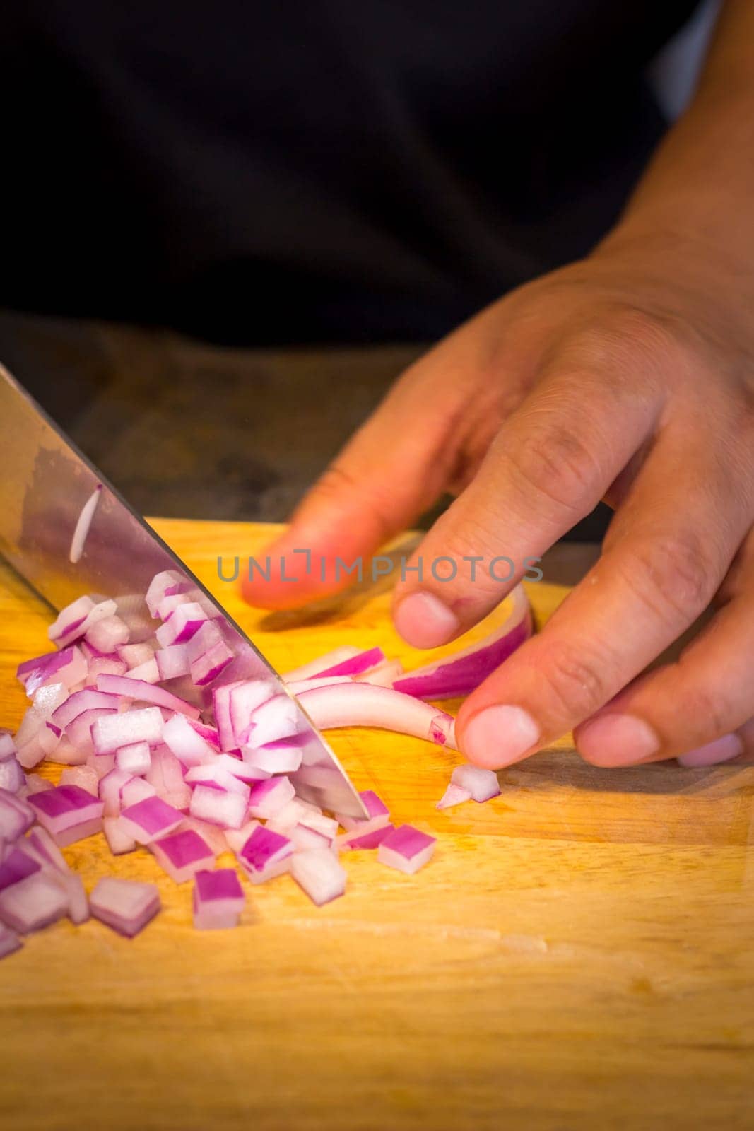 Chef chopping a red onion with a knife on the cutting board.