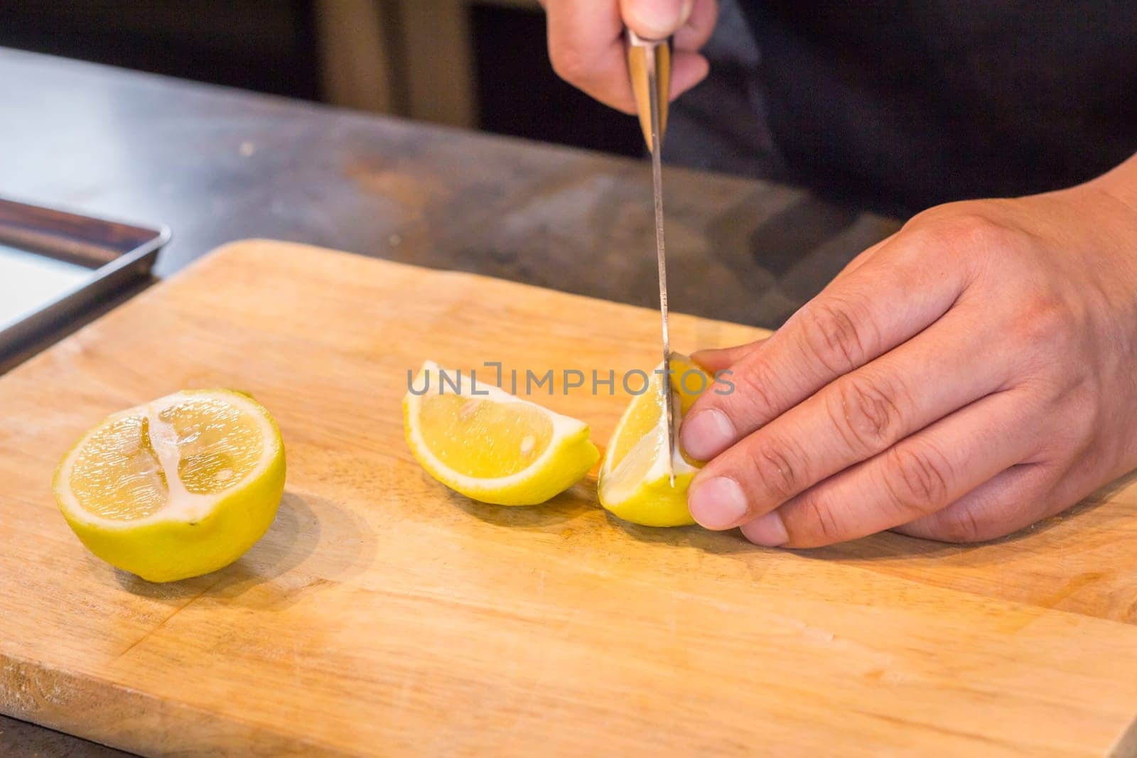 Chef slicing Lemon on wooden cutting board.