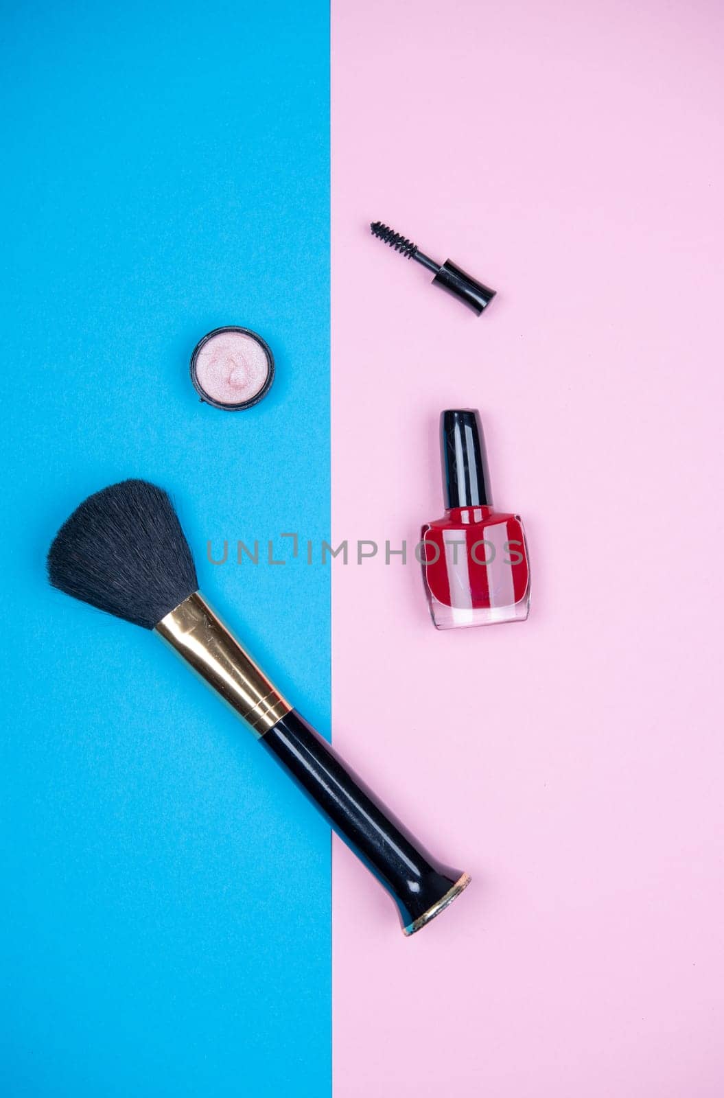 makeup collection with  mascara, nail polish ,eye shadow and brush from above on blue and pink ground