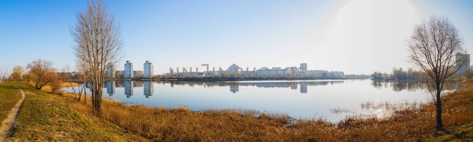 Panoramic shot of large lake. Coastline, the reflection of buildings in calm water.