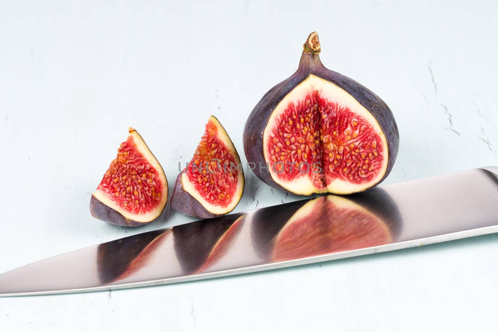 A whole with a cutout and small piece of ripe, delicious and sweets figs with a kitchen knife on a light blue vintage background