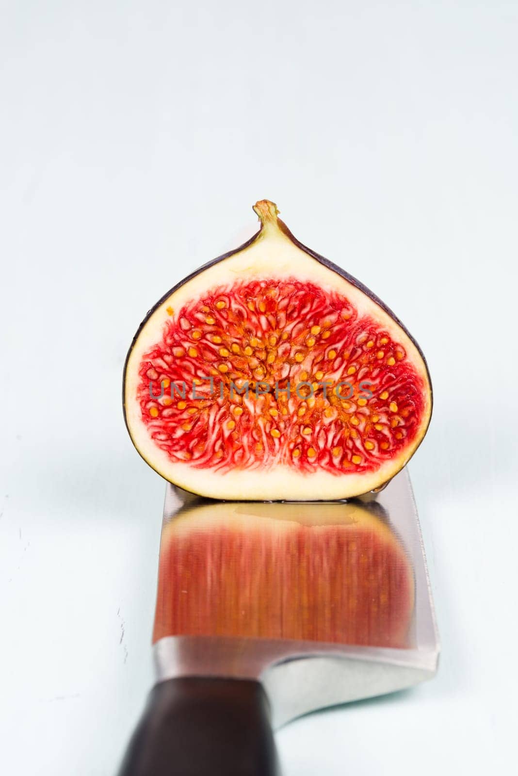 One whole ripe and sweet fig with a cutout is on a kitchen knife with refelction on a light blue vintage background