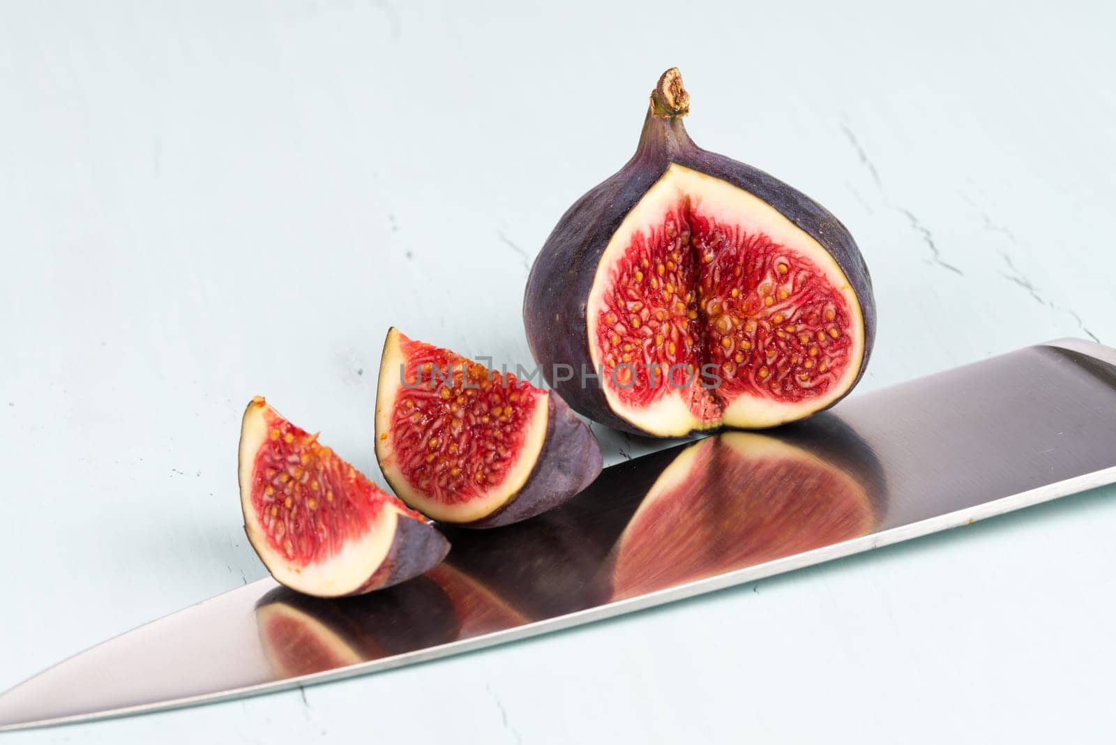 A whole with a cutout and small piece of ripe, delicious and sweets figs with a kitchen knife on a light blue vintage background