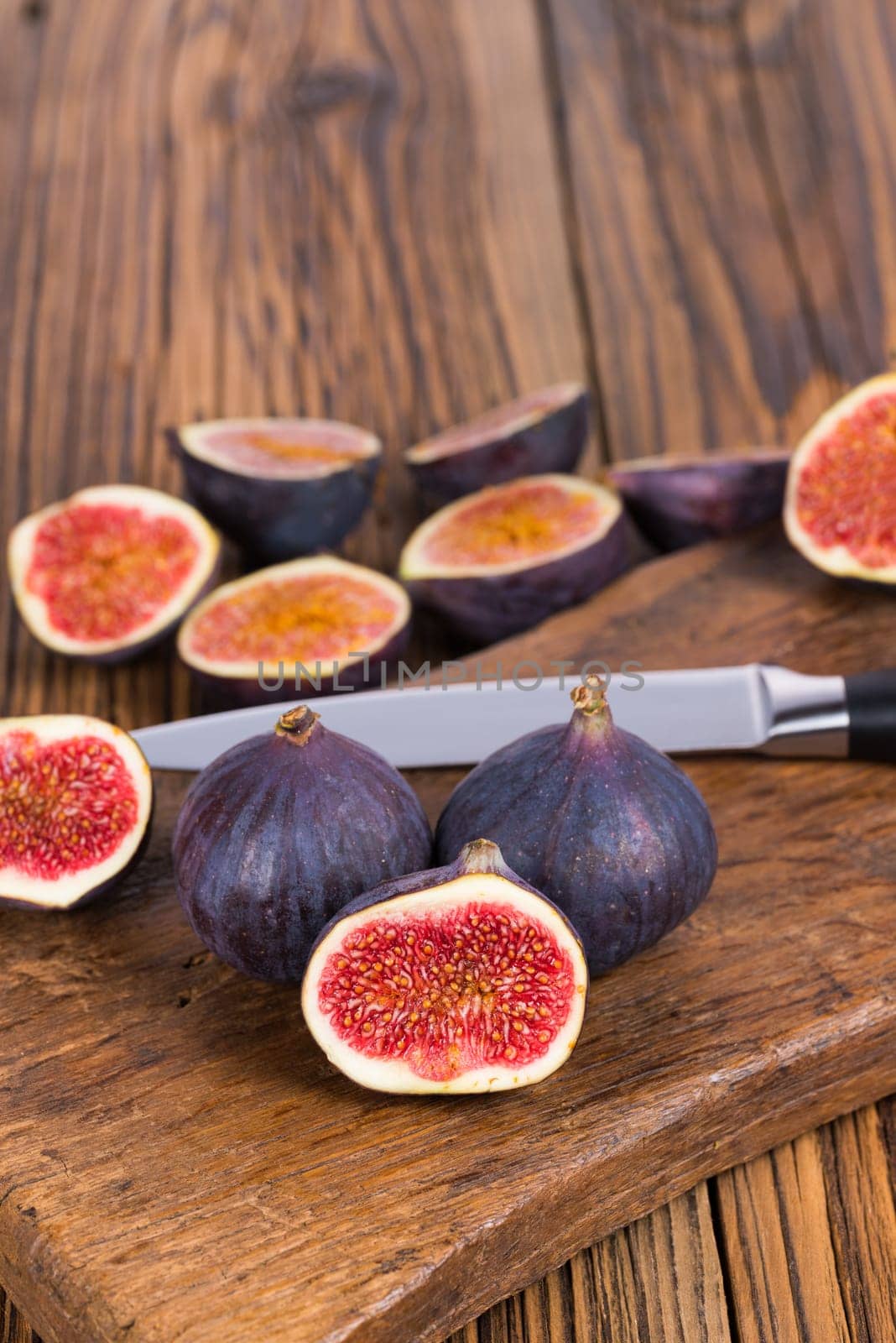 Group of whole and sliced ripe, delicious and sweets figs with a kitchen knife on a old rustic wooden cutting board with copy space in upper picture area