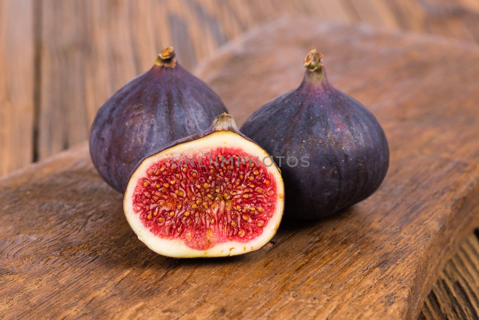 Two whole and one half delicious and sweets figs on a rustic wooden background