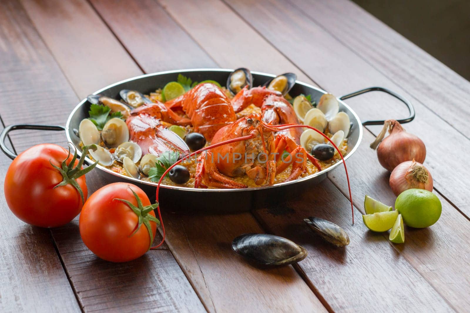 Gourmet seafood Valencia paella with fresh langoustine, clams, mussels and squid on savory saffron rice with peas and lemon slices, close up view